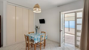 Un'area pranzo con tavolo e sedie, un lampadario, un televisore appeso al muro e una porta che dà su un balcone esterno.