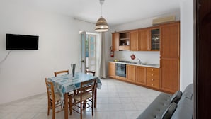 Una cucina compatta con mobili in legno, un tavolo da pranzo con sedie e una TV a incasso.