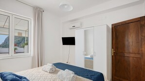 Hotellihuone, jossa on sänky, seinälle asennettu televisio, puuovi ja ikkuna, jossa on verhot.