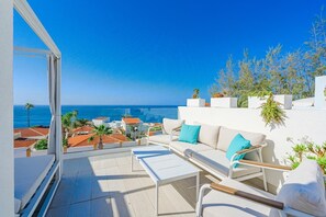 A balcony with a white sofa, a small table, and potted plants.