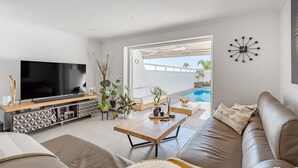 A modern living room with a flat-screen TV, a sofa, a coffee table, and a pool visible through the glass door. - Vacation Home 'La Perla' with Sea View, Wi-Fi and Air Conditioning (Callao Salvaje)