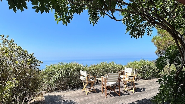 Eine Holzterrasse mit Gartenmöbeln, mit Blick auf einen klaren blauen Himmel und das Meer.