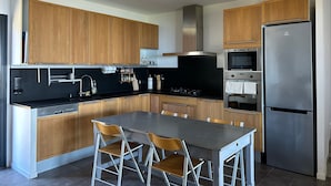 Eine moderne Küche mit Holzschränken, einem Edelstahlkühlschrank, einem Einbauofen und einem Esstisch mit Stühlen.