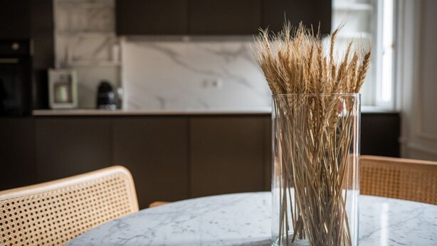 A clear glass vase with dried grasses on a marble table in a modern kitchen with dark cabinetry and a wicker chair. - La Casa di Gylda - luxe flat (Milano)