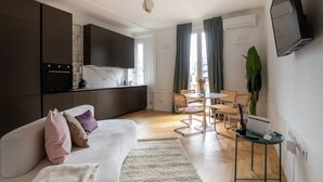 A modern living room with a sofa, a dining area with a table and chairs, a kitchen with dark cabinets, and a flat-screen TV mounted on the wall. - La Casa di Gylda - luxe flat (Milano)