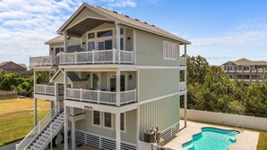 A two-story house with a balcony, a pool, and a staircase leading to the upper floor. - 7240- Island Oasis - Dog-Friendly Salvo Home w/ Pool & Hot Tub (Salvo)