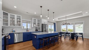 A modern kitchen with blue cabinetry, stainless steel appliances, and a central island with bar stools. - 7240- Island Oasis - Dog-Friendly Salvo Home w/ Pool & Hot Tub (Salvo)