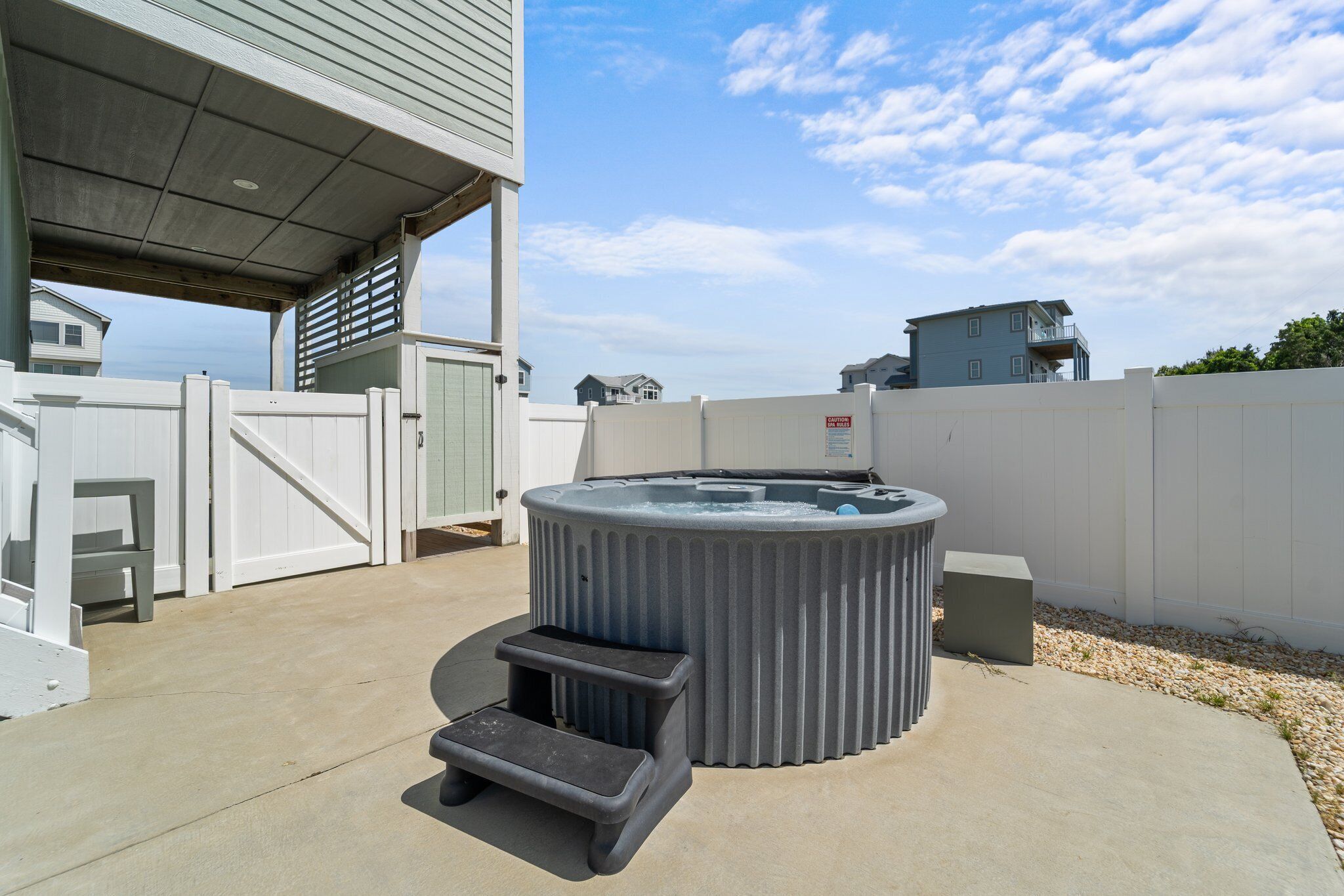 A hot tub with steps, a covered patio, and a white fence.