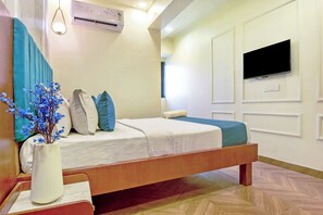 A hotel room with a bed, a TV mounted on the wall, and a vase with flowers on the nightstand.