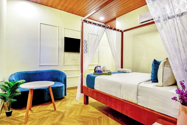A bedroom with a four-poster bed, a blue sofa, a small round table, and a potted plant.