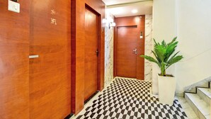 A hotel hallway with wooden doors, a checkered floor, a marble wall, and a staircase with a potted plant. - THE Solitaire Residency  (Kalyan)