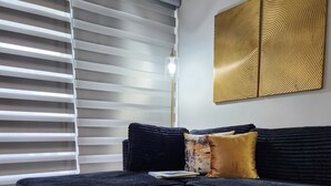 Une chambre à coucher moderne avec un canapé bleu foncé, un plateau en bois avec des bougies et une grande fenêtre avec des stores.