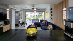 Un salon moderne avec un canapé noir, un bol doré posé sur une table noire et un téléviseur sur un meuble en bois.