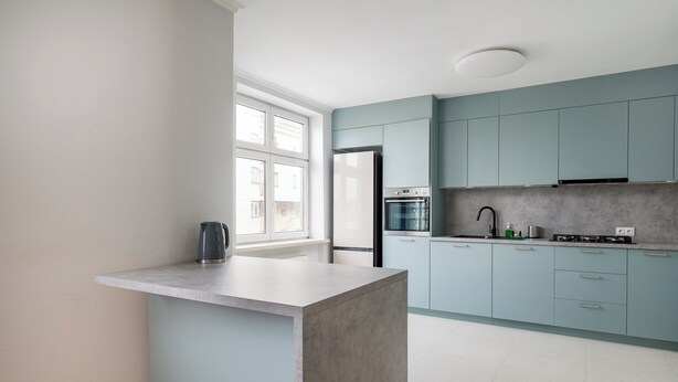 Una cocina moderna con una isla central, armarios azul claro y un ventanal que proporciona luz natural.