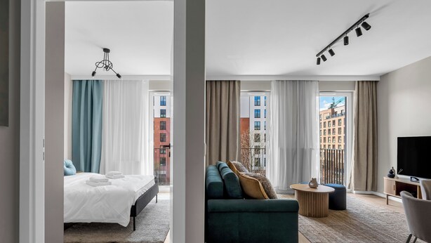 Ett modernt hotellrum med en säng, en soffa, en TV och en balkong med utsikt över staden.