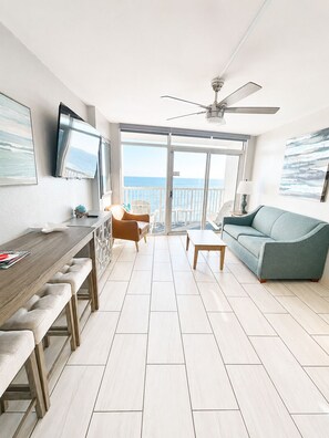 A modern living room with a dining area, a sofa, a TV, and a balcony with a view of the ocean. - Newly Renovated 1 Bedroom Beach Condo at SeaWatch Resort Myrtle Beach (Myrtle Beach)