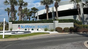 The entrance to SeaWatch Resort with a sign, palm trees, and a parking garage in the background. - Newly Renovated 1 Bedroom Beach Condo at SeaWatch Resort Myrtle Beach (Myrtle Beach)