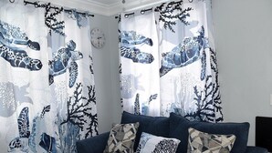 Un salon avec un canapé bleu foncé, des coussins à motifs et des rideaux ornés d’un motif abstrait bleu et blanc.