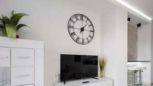 A modern living room with a white entertainment unit, a flat-screen TV, a large wall clock, and a small plant. - Riverside Harmony Chic Apartment (Wrocław)