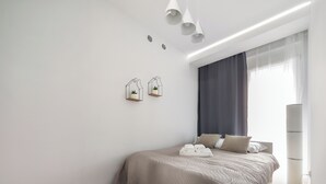 A modern bedroom with a bed, a bedside table, a lamp, and a window with curtains. - Riverside Harmony Chic Apartment (Wrocław)