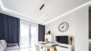 A modern living room with a dining area, a sofa, a flat-screen TV, and a large wall clock. - Riverside Harmony Chic Apartment (Wrocław)