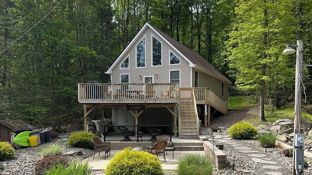 Une cabane à deux étages dotée d’un balcon, entourée d’une allée en gravier et d’un jardin aménagé.