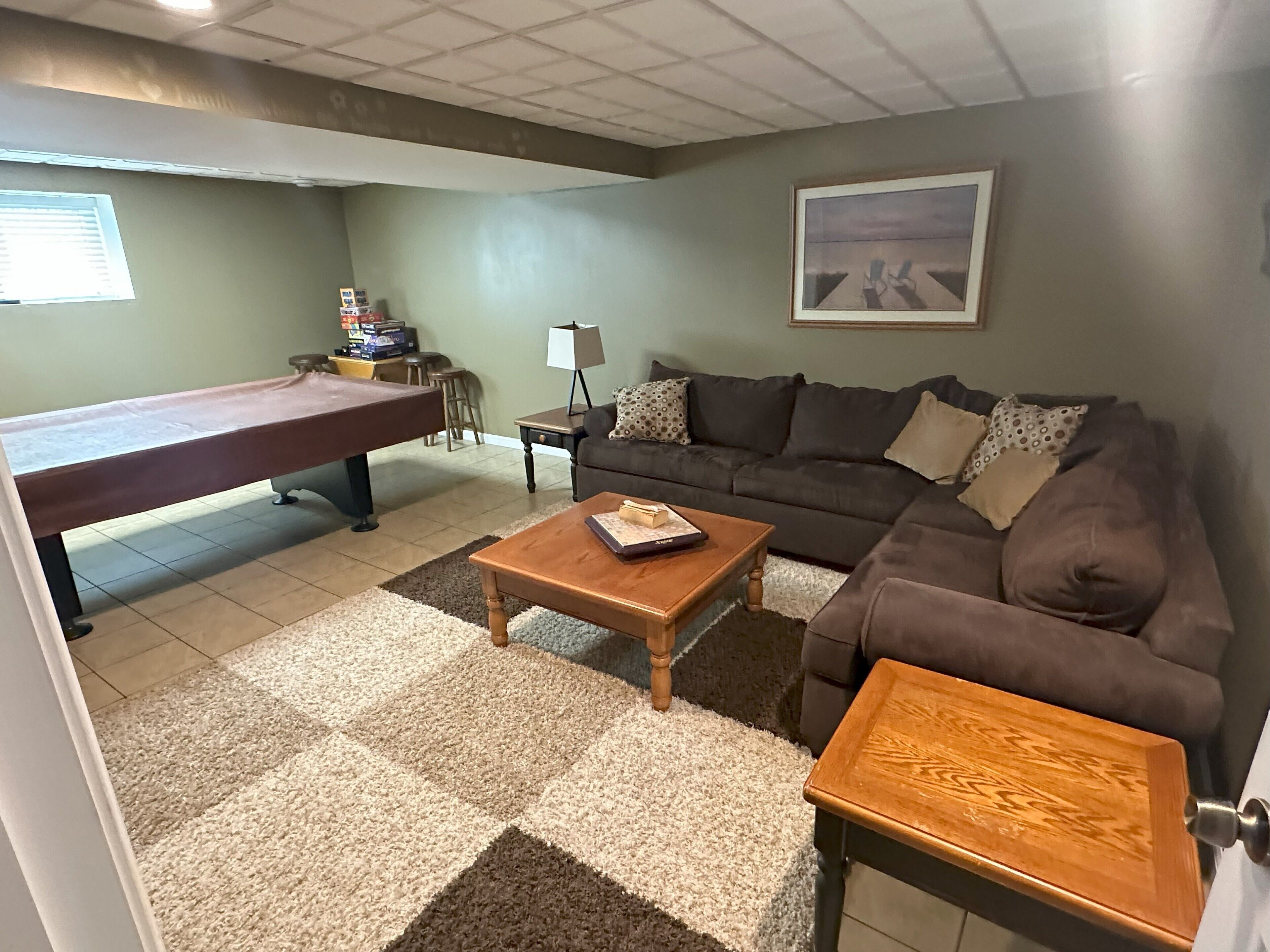 A living room with a pool table, a sofa, a coffee table, and a painting on the wall.
