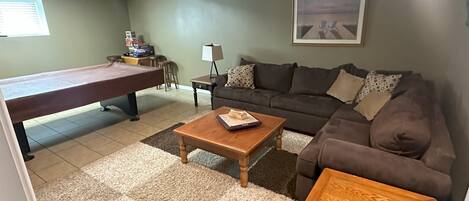 A living room with a pool table, a sofa, a coffee table, and a painting on the wall.