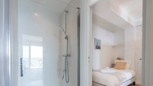 Une salle de bain moderne avec une douche à parois de verre, un lit avec une literie blanche et un plancher en bois.