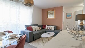 A modern living room with a grey sofa, a dining table with chairs, and a kitchen area with a stove. - Terra Tosca by Interhome (Fréjus)