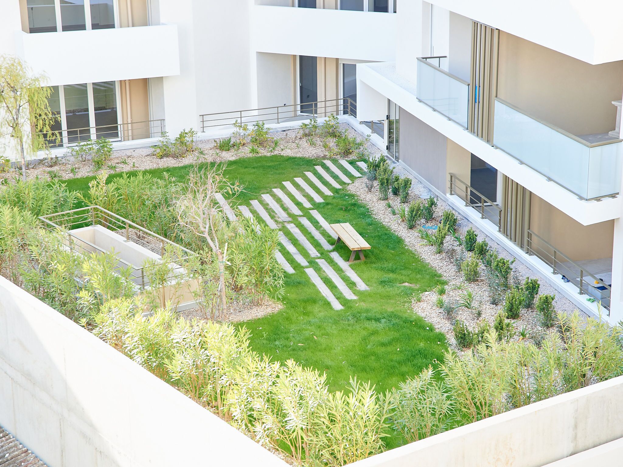 Een modern gebouw met een dakbostuin, inclusief een houten bankje, een kleine vijver en diverse planten.
