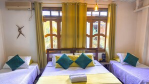 Une chambre d’hôtel avec deux lits, chacun recouvert d’une courtepointe blanche matelassée et agrémenté d’oreillers turquoise. On y trouve une fenêtre avec des rideaux jaunes, un luminaire suspendu et un climatiseur fixé au mur.