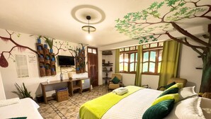 Une chambre à coucher comprenant un lit, un bureau, une chaise, un téléviseur et un mur décoré d’une fresque représentant un arbre.
