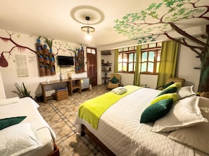 Un dormitorio con cama, escritorio, silla, televisión y un mural de un árbol en la pared.