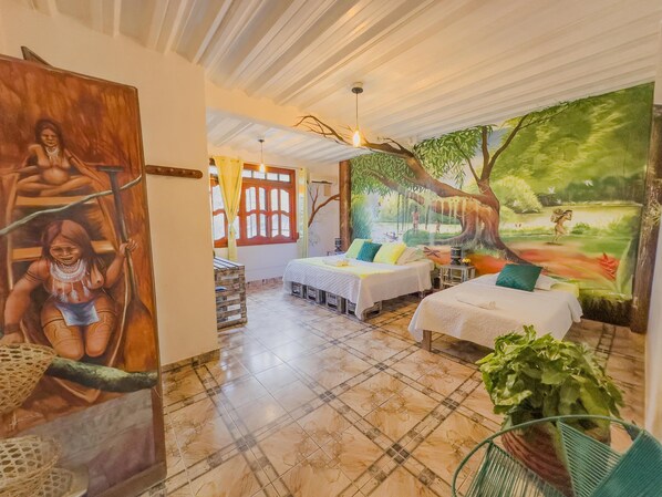 A room with two beds, a large mural, and a view of a forest.