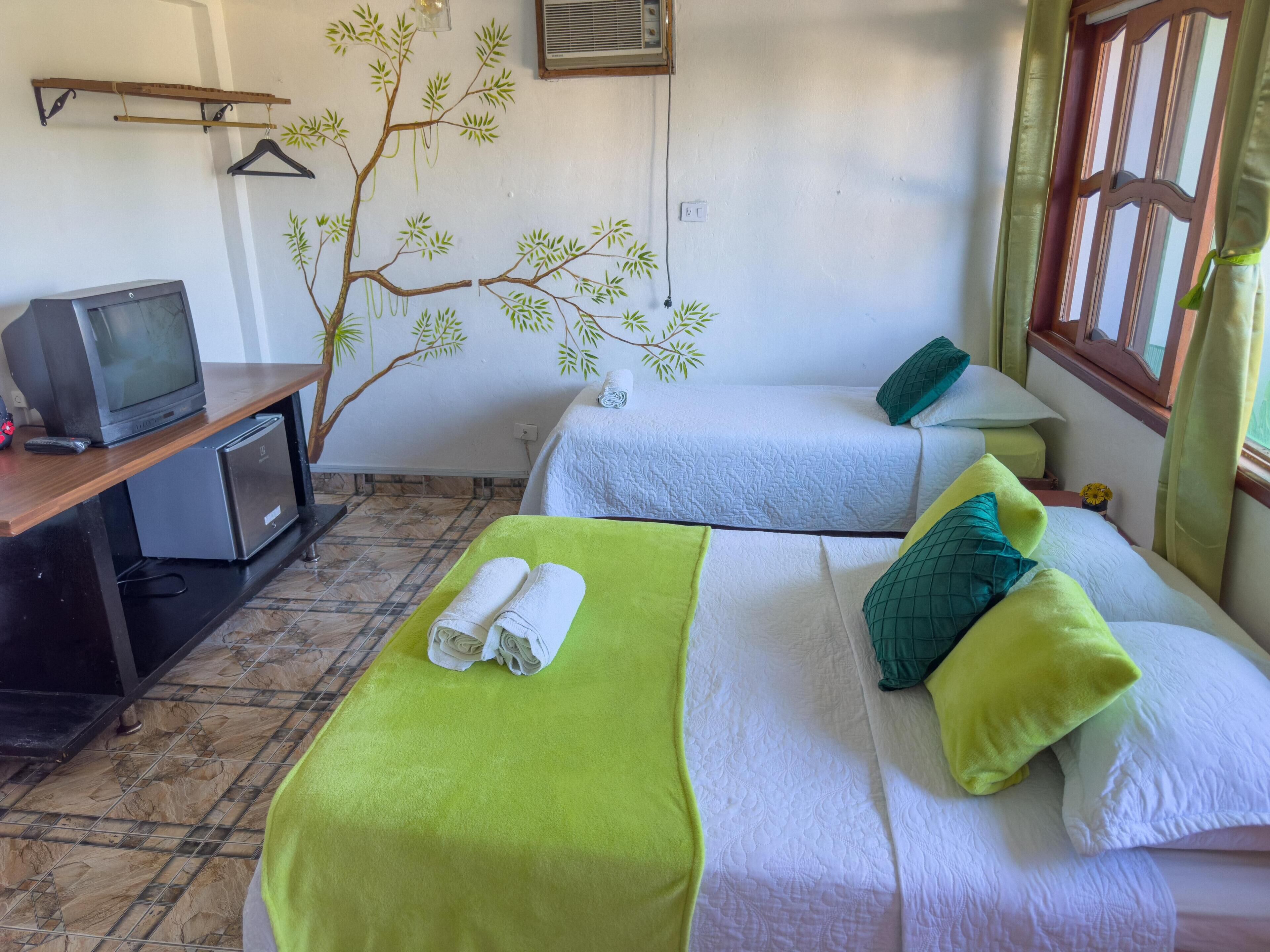 Une chambre d’hôtel avec deux lits, une télévision, un petit bureau et un mur décoratif représentant des arbres.