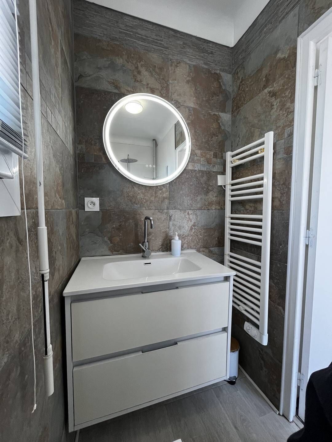 A modern bathroom with a white vanity, a round mirror, and a towel rack.