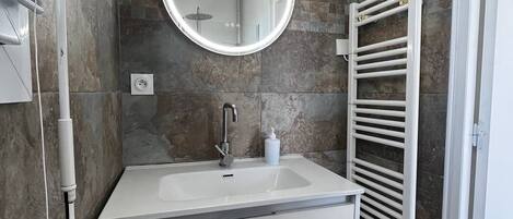 A modern bathroom with a white vanity, a round mirror, and a towel rack.