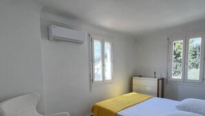 A bedroom with a checkered floor, a bed with white bedding, a chair, and an air conditioning unit. - Charming Canet House Close to the Beach and Amenities! (CANET PLAGE)