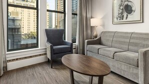 Una sala de estar moderna con un sofá gris, un sillón a juego y una mesa de centro de madera. Una lámpara y un cuadro enmarcado decoran la pared.