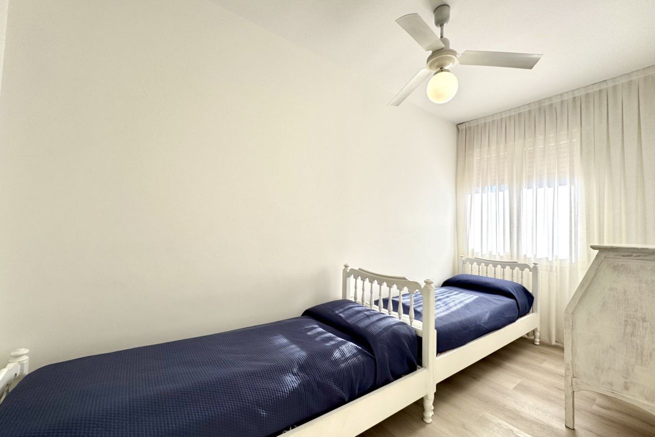 A single bed with a white frame and dark blue bedding in a room with white walls and a ceiling fan.