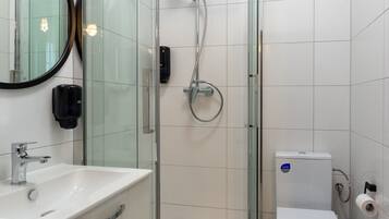 Un baño moderno con ducha envuelta en vidrio, un lavamanos blanco y un inodoro.