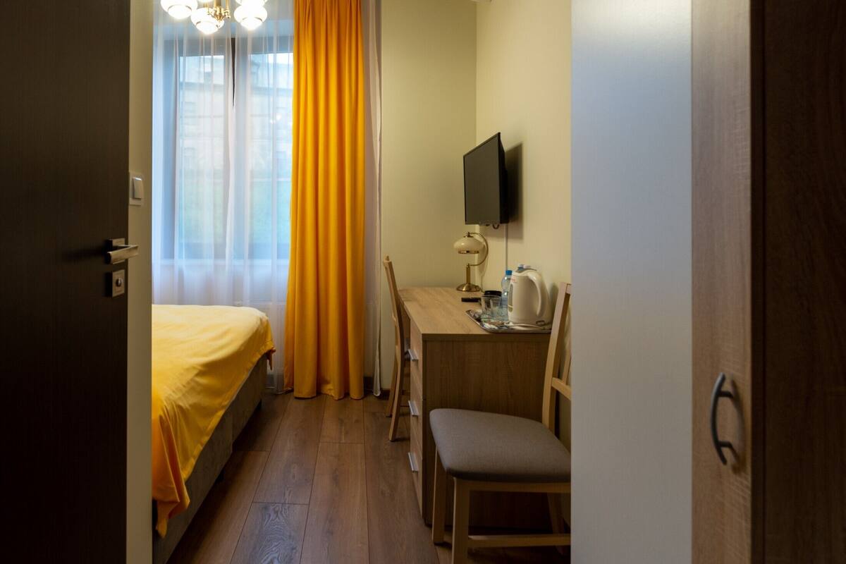A hotel room with a bed, a desk, a chair, a television, and a window with curtains.