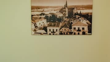 Un lit avec une literie blanche et deux coussins jaune vif, et au-dessus, un tableau encadré représentant une ville.