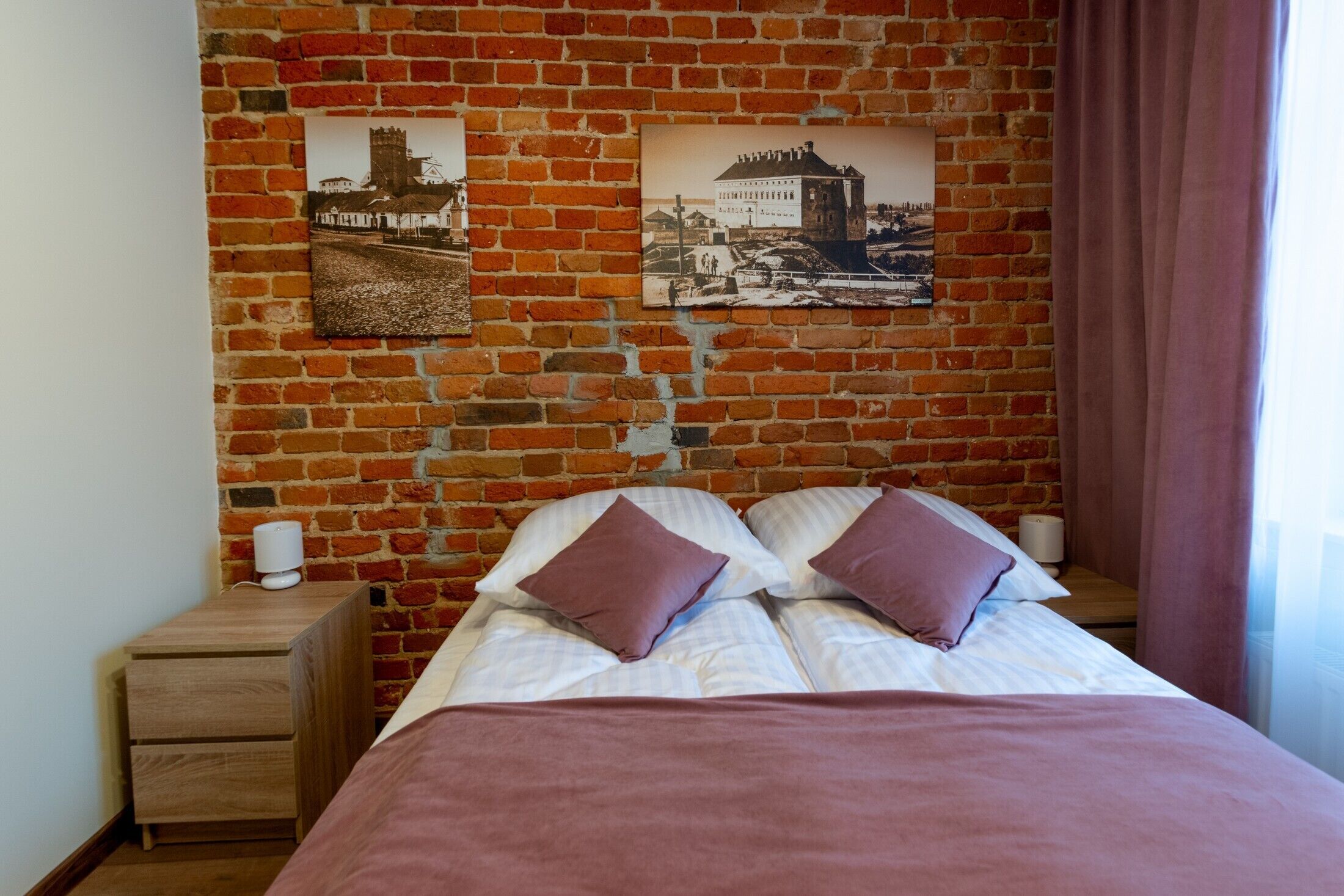 Ein Schlafzimmer mit Backsteinwand, einem Bett mit zwei Kissen, einem Nachttisch und zwei gerahmten Bildern.