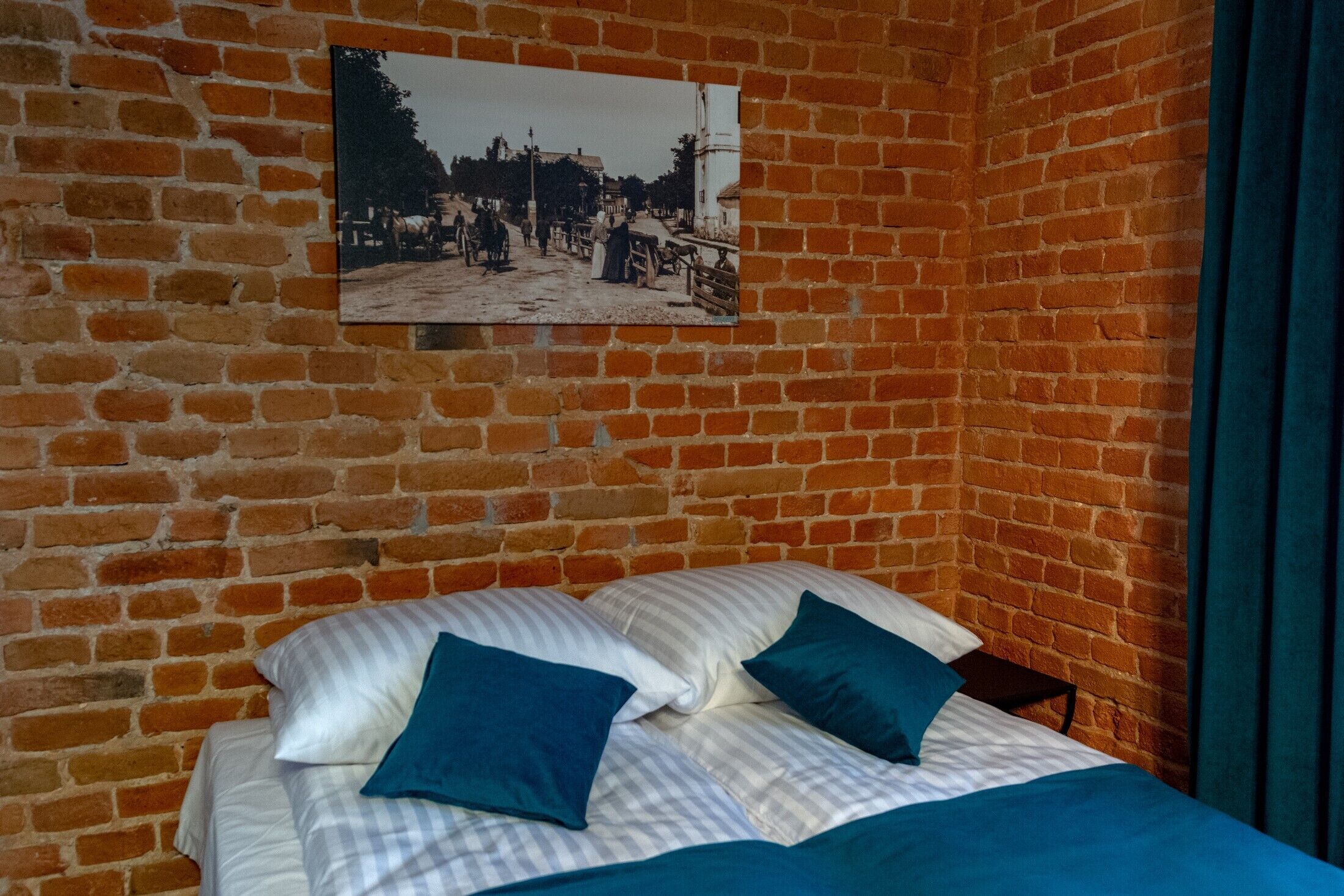 Een kamer met een bakstenen muur, een bed met gestreepte beddengoed en twee kussens, en een lijst met een afbeelding boven het bed.