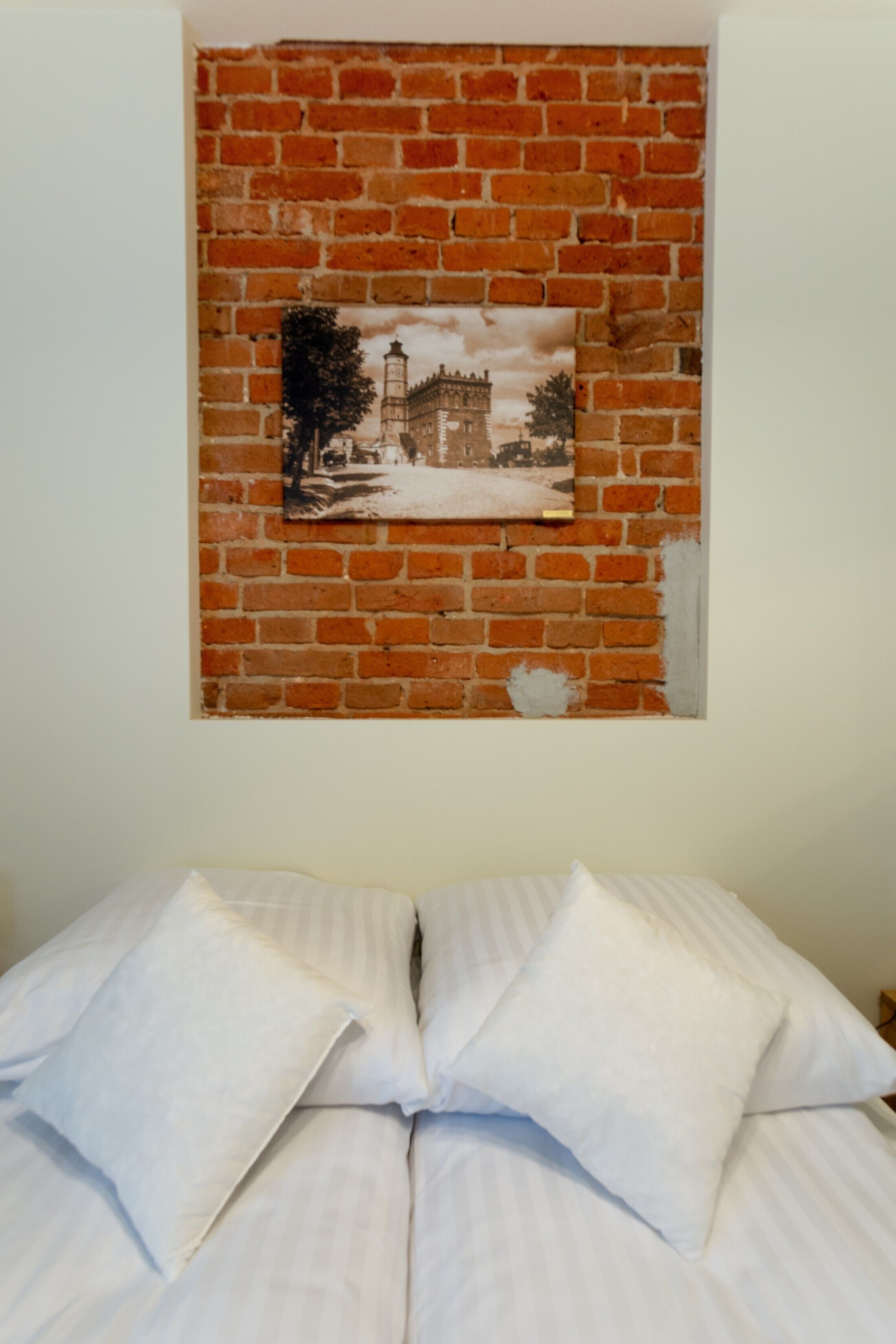 A bed with white linens and pillows, a brick wall, and a framed picture of a building.