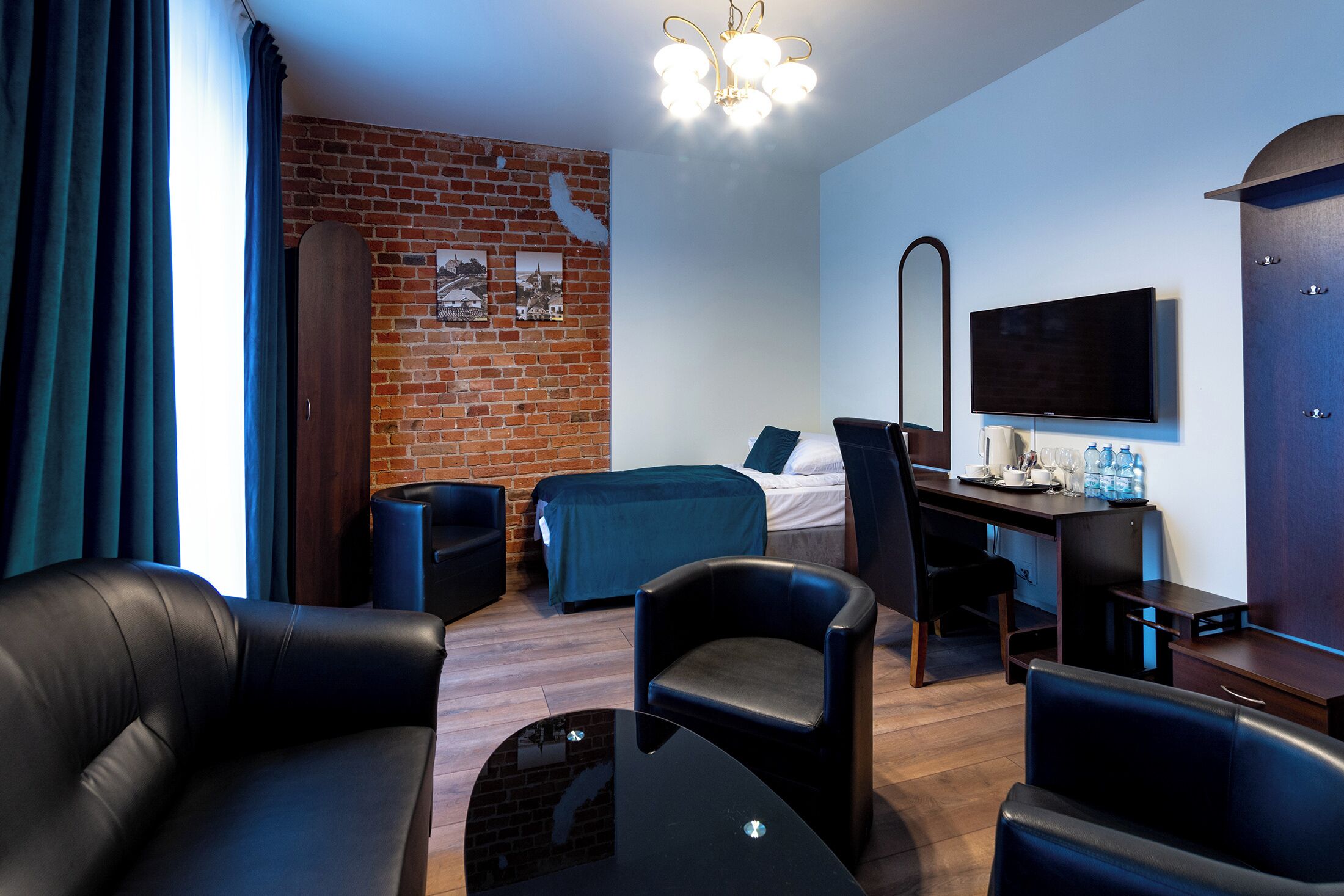 Une chambre d’hôtel moderne avec un mur en briques, un lit, un bureau avec une chaise, une télévision et un canapé.