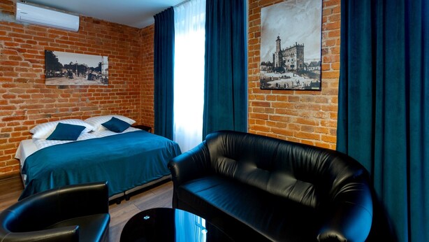 Une chambre d’hôtel avec un mur en briques, un lit avec une literie bleue, un canapé en cuir noir et deux fauteuils.