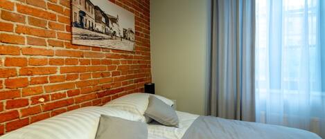 A hotel room with a brick wall, a bed with white linens, a framed picture, and an air conditioning unit.